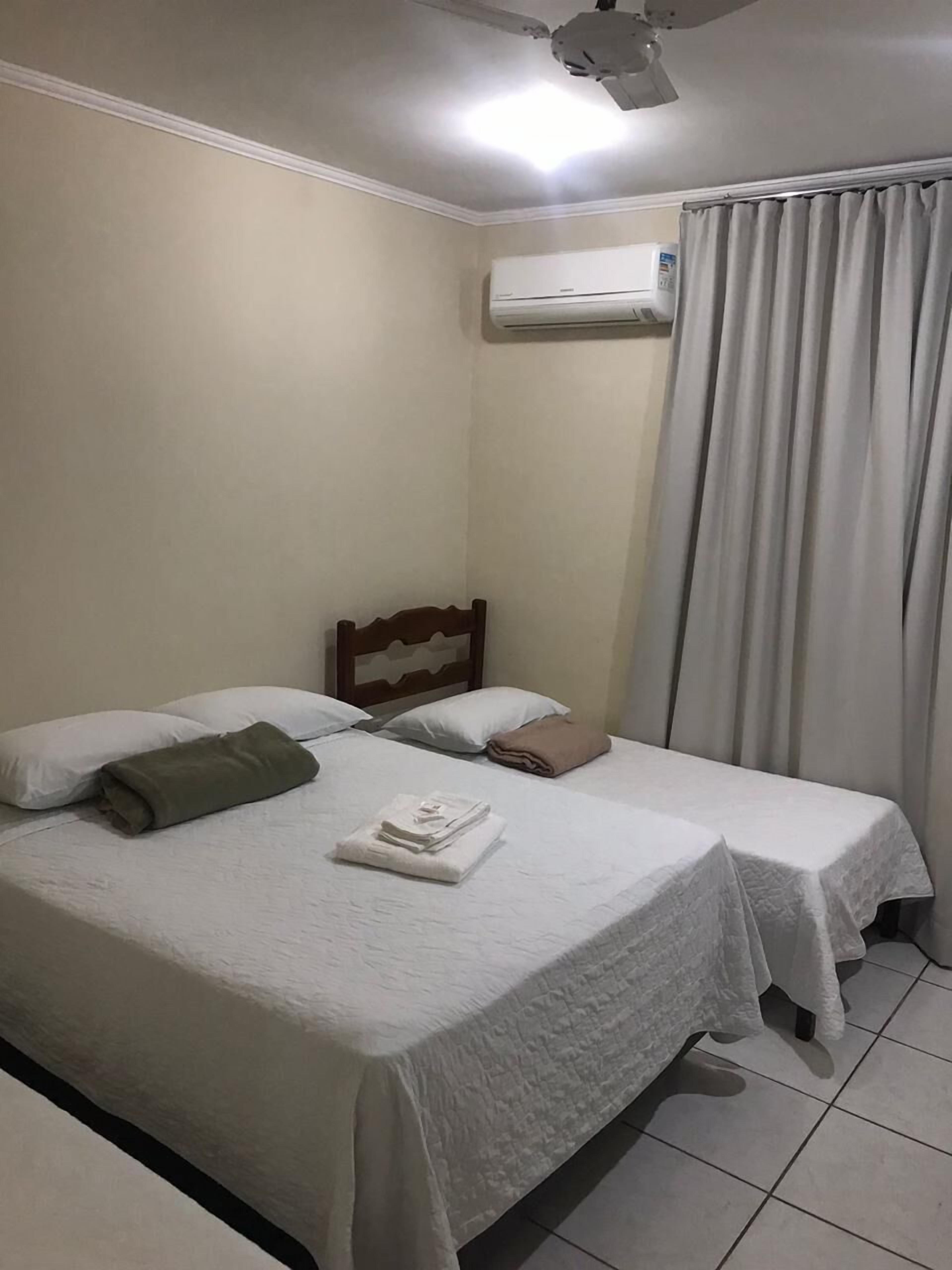 A hotel room with two beds, a ceiling fan, an air conditioning unit, and a window with curtains.