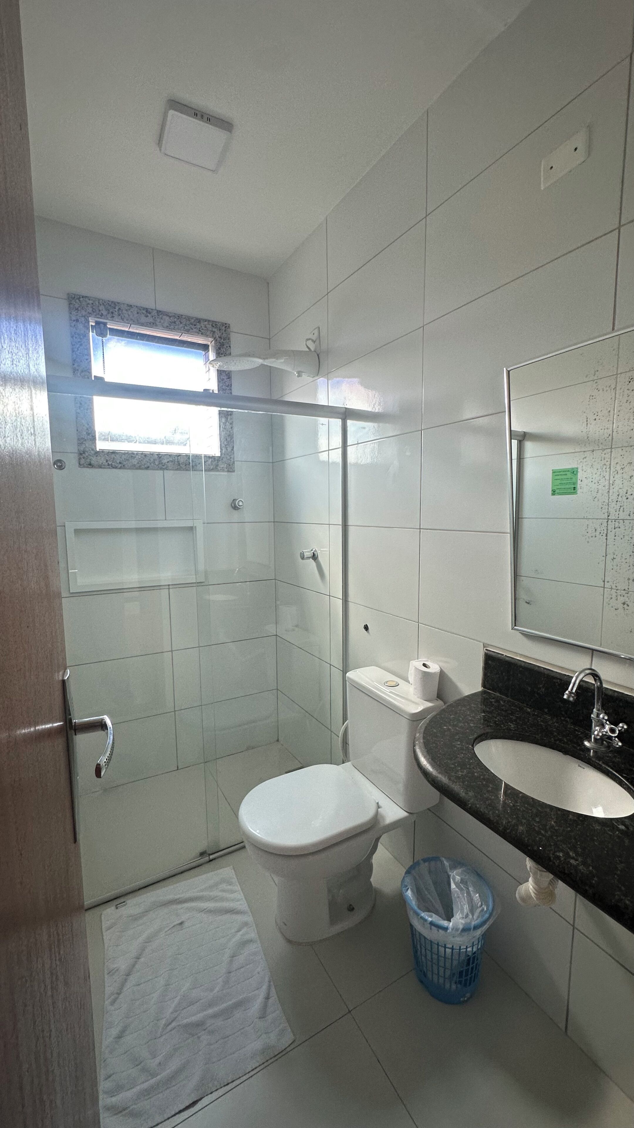 A bathroom with a toilet, sink, shower, and a window.