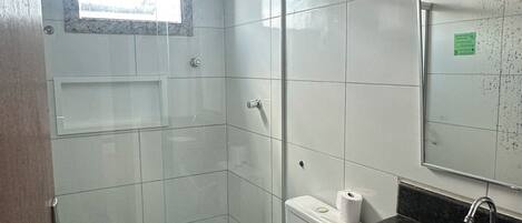 A bathroom with a toilet, sink, shower, and a window.
