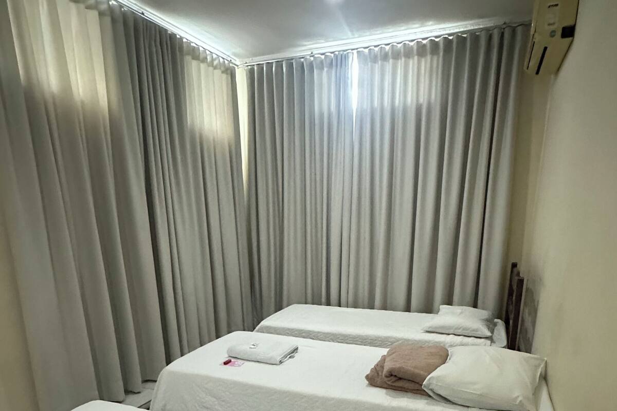 A hotel room with two beds, a ceiling fan, and a window with curtains.