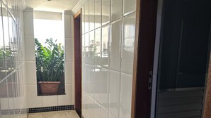 A corridor with tiled walls and floor, a potted plant, and a door. - GV Park Hotel (Governador Valadares)