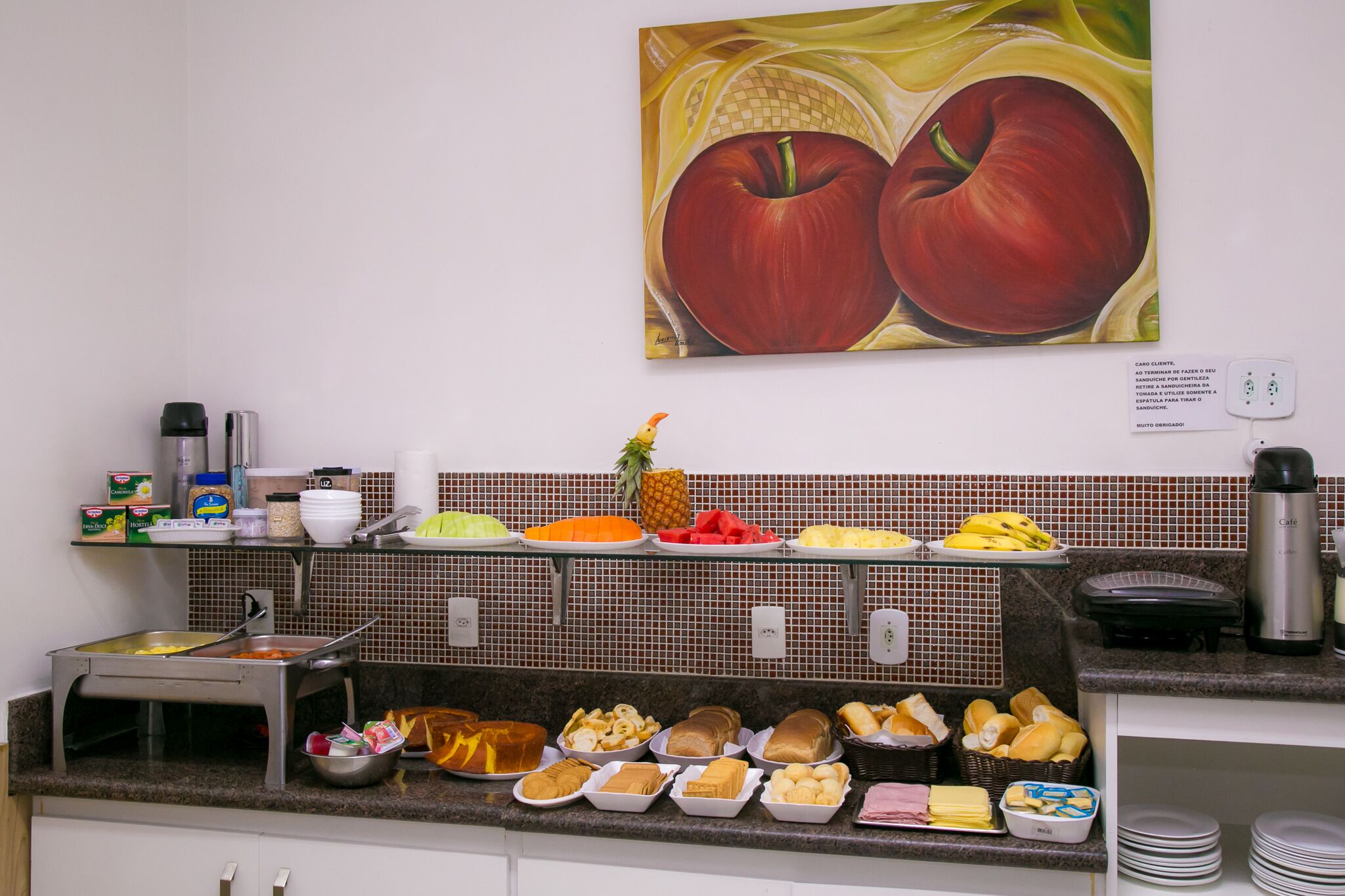 A buffet setup with various food items and a painting of apples on the wall.