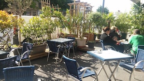 An outdoor seating area with tables and chairs, surrounded by potted plants and trees. - La Caravelle (Riom)