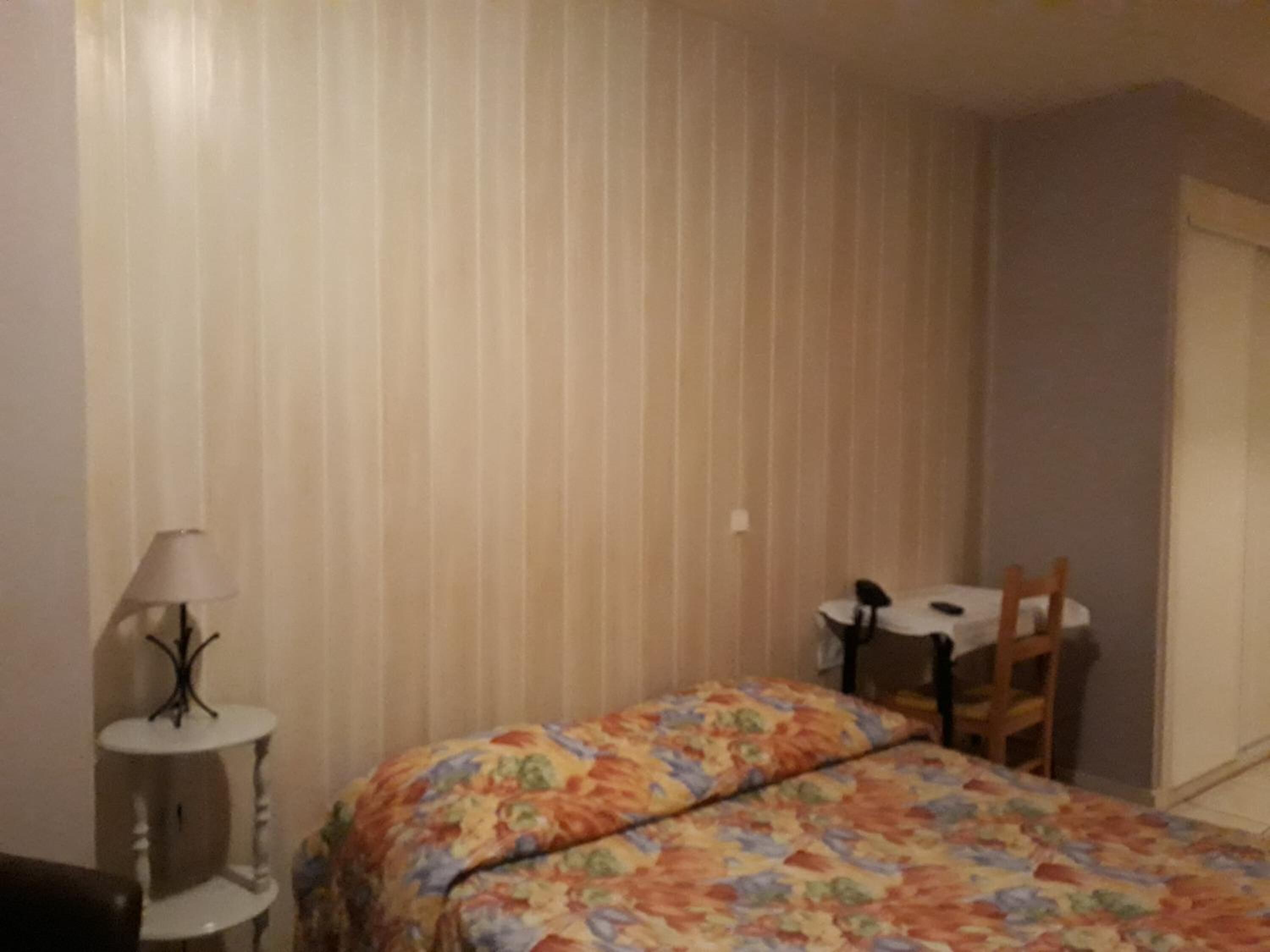 Una stanza con un letto, una sedia, un tavolino e una lampada.