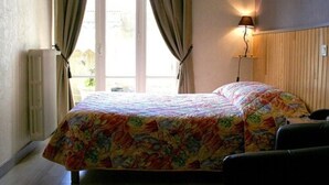 A bedroom with a bed, curtains, a lamp, and a radiator. - La Caravelle (Riom)