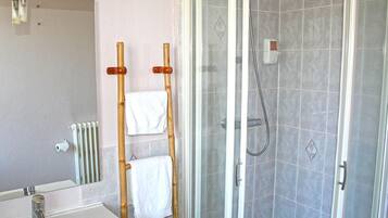 Une salle de bain avec un lavabo blanc, un miroir, une douche avec une porte en verre et un porte-serviettes avec deux serviettes blanches.