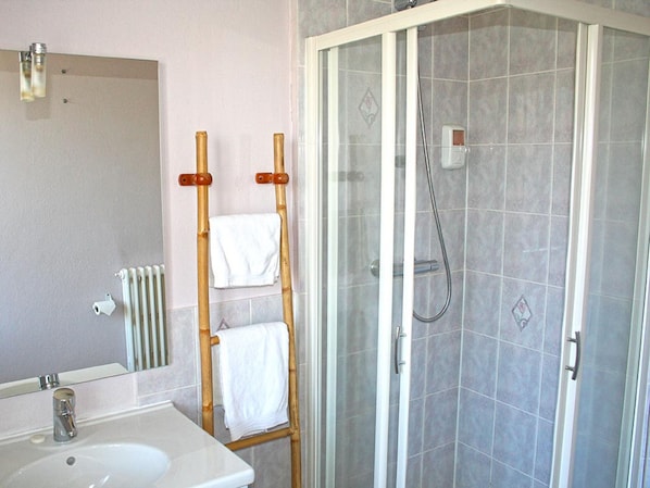A bathroom with a white sink, a mirror, a shower with a glass door, and a towel rack with two white towels. - La Caravelle (Riom)