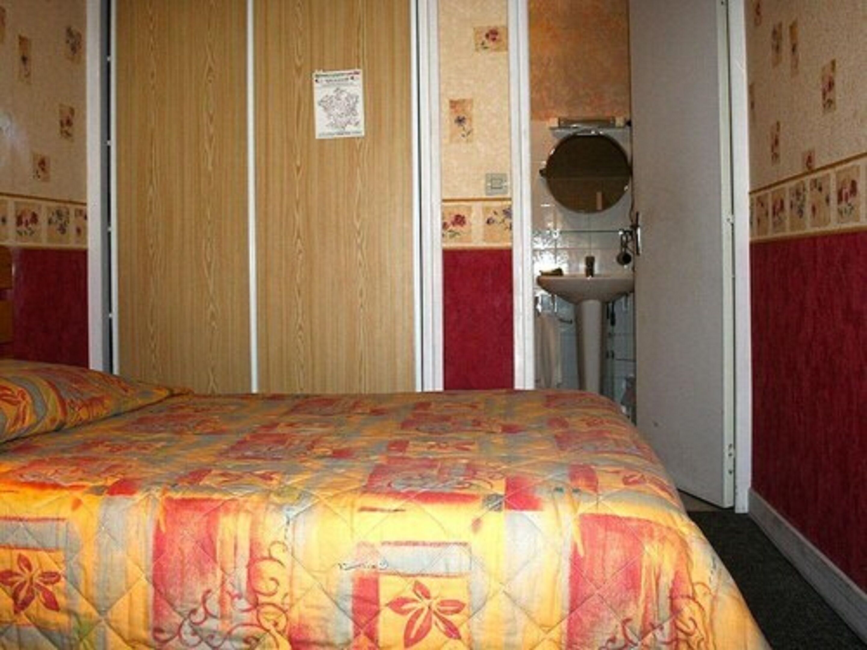 Un dormitorio con cama, armario de madera y baño con lavamanos y espejo.