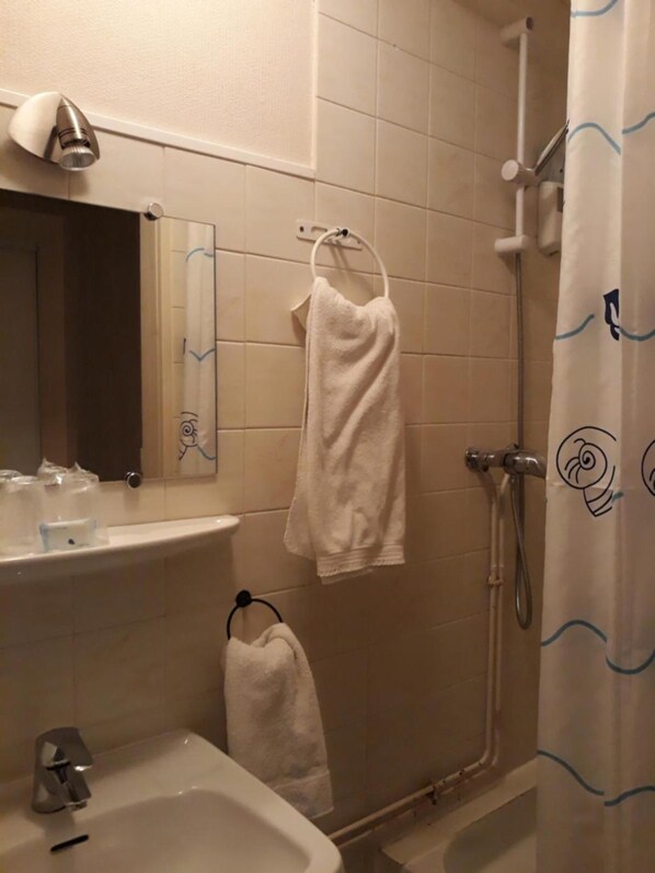 A bathroom with a sink, mirror, towel rack, and shower curtain. - La Caravelle (Riom)
