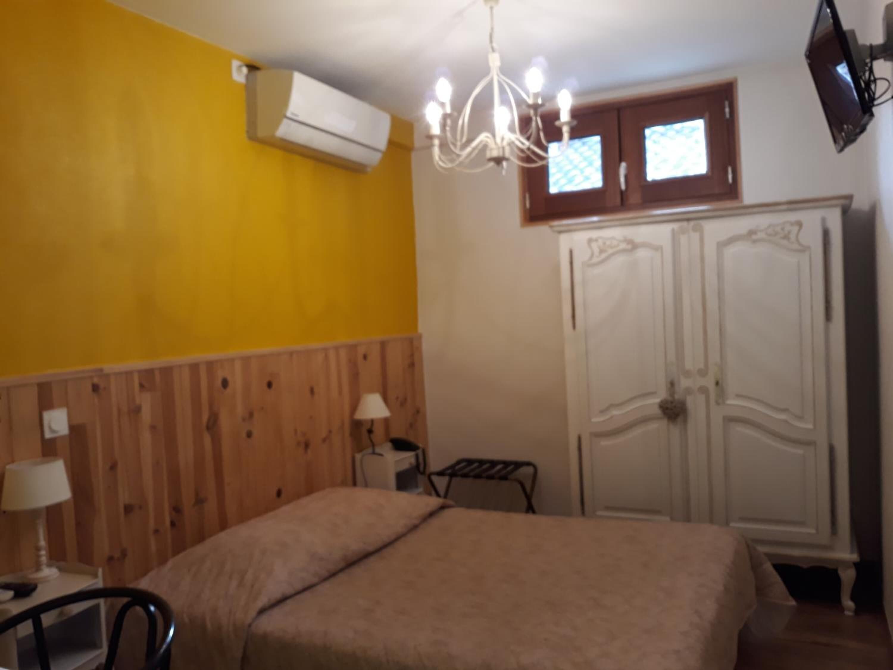A room with a bed, a wooden headboard, an air conditioning unit, a chandelier, a wardrobe, and a television.