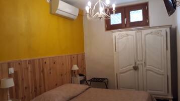 A room with a bed, a wooden headboard, an air conditioning unit, a chandelier, a wardrobe, and a television.