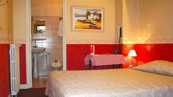 Een hotelkamer met een bed, een nachtkastje, een lamp, een schilderij aan de muur en een badkamer door een open deur zichtbaar.