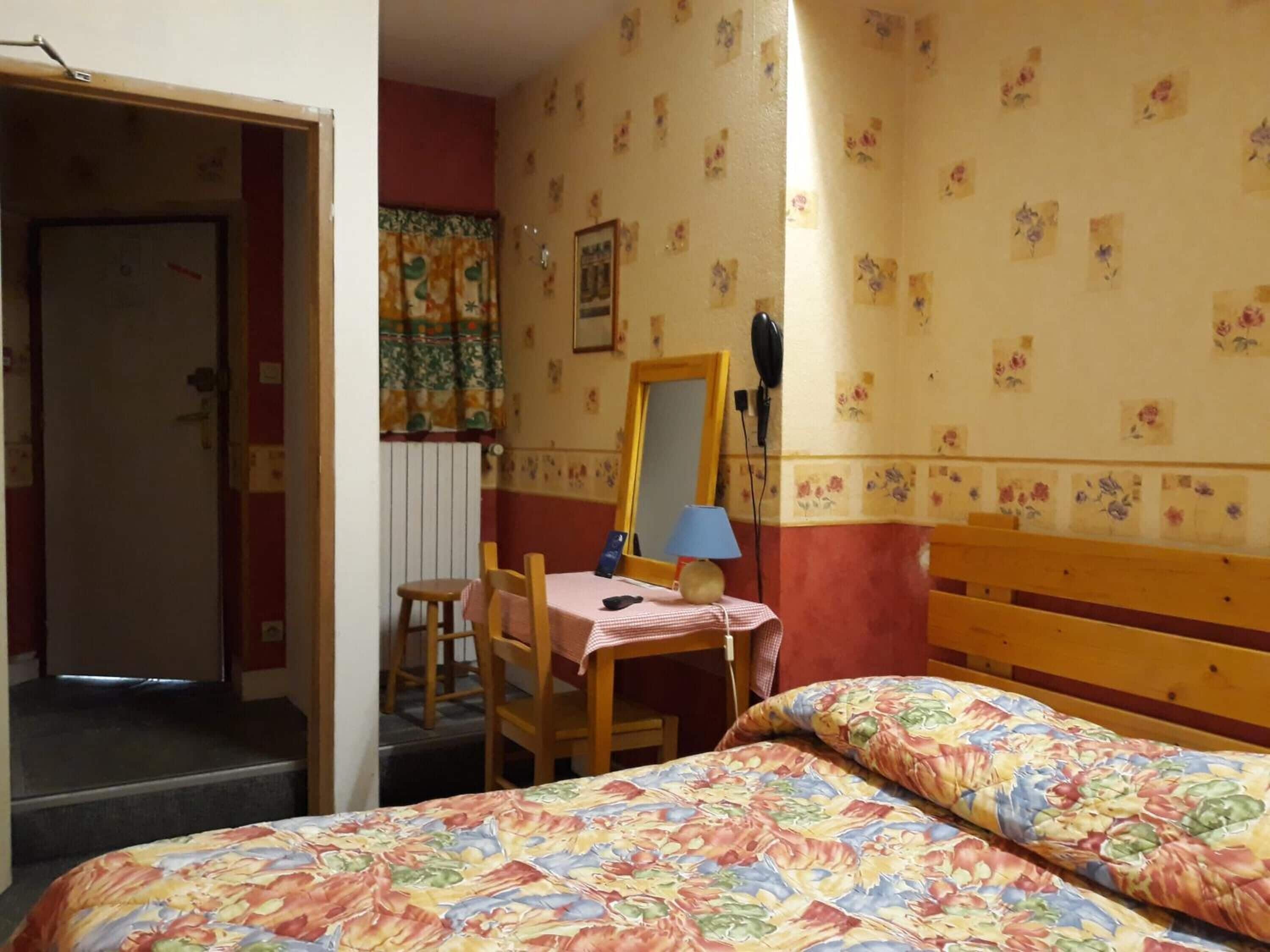 A room with a bed, a chair, a table with a lamp, and a mirror.