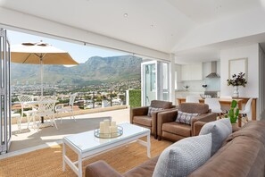 Un soggiorno moderno con un tavolo in vetro, due divani e un'area pranzo con sedie. Un'ampia finestra offre vista su un paesaggio montuoso.