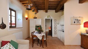 A cozy kitchen with a dining table, chairs, and a red lamp. There is a window with a view, a wooden ceiling, and a white cabinet. - Apartment BERRIES (Agriturismo Il Corniolo) (CORCIANO)