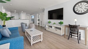 A modern living room with a sofa, coffee table, TV, and a dining area with a chair and table. - Brand New Premium Ocean View 3 Bedroom Condo w/ On-Site Rental Privileges (Myrtle Beach)