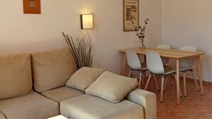 A living room with a sofa, a dining table with chairs, a wall-mounted light, and a framed picture. - BURGIT - Modern apartment located 80 metres from the paradisaical cove of Cala Barca Trenc (Santanyí)