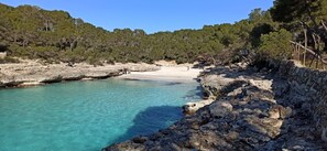 A rocky coastline with clear turquoise water and a sandy beach.