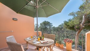 A balcony with a table set for breakfast, chairs, a green umbrella, and potted plants. - BURGIT - Modern apartment located 80 metres from the paradisaical cove of Cala Barca Trenc (Santanyí)
