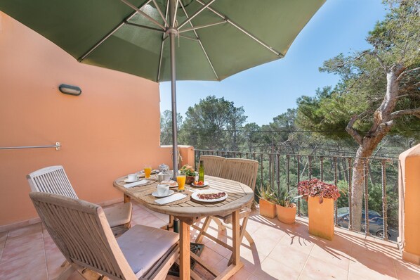 A balcony with a table set for breakfast, chairs, a green umbrella, and potted plants.