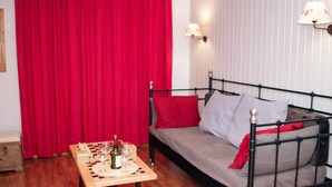 Ein Zimmer mit einem Bett, einem Holztisch mit Schachfiguren und Weingläsern sowie einem roten Vorhang.