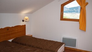 Ein Schlafzimmer mit einem Holz-Kopfteil, einem Bett mit brauner Bettwäsche, einem Nachttisch, einem Fenster mit Vorhängen und einer wandmontierten Klimaanlage.