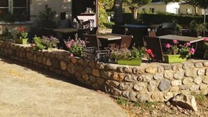 A building with a sign reading "ACCUEIL" indicating a reception area. There is a stone wall with potted plants and outdoor seating. - Camping La Charderie (Pont-de-Labeaume)