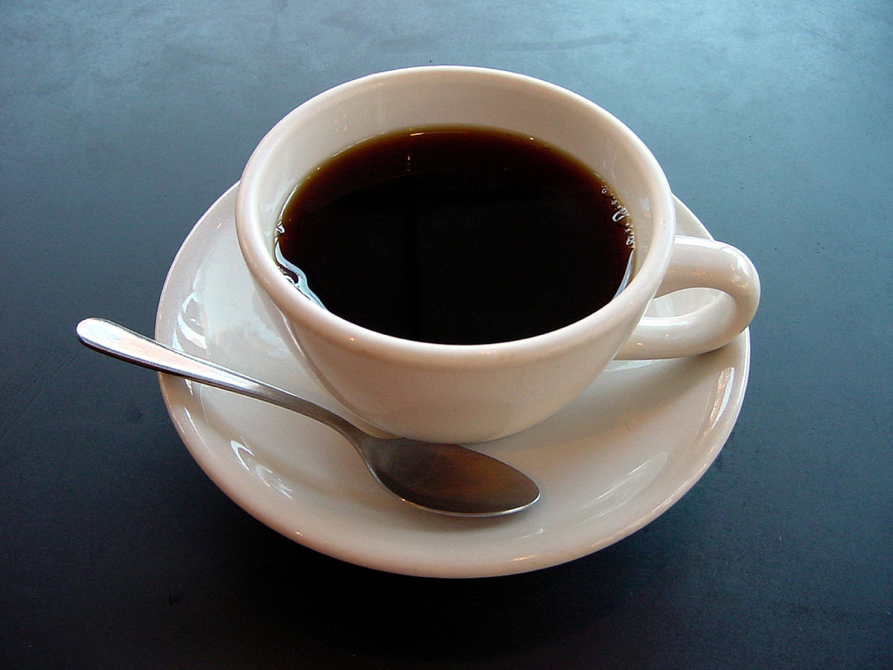 A white cup of coffee on a saucer with a spoon, placed on a table.
