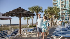 A beachside hotel with lounge chairs, umbrellas, and palm trees. - Gorgeous Modern Ocean View Condo w/ Access to Resort Amenities (Myrtle Beach)