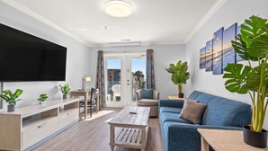 A modern living room with a flat-screen TV, a blue sofa, a wooden coffee table, and potted plants. - Gorgeous Modern Ocean View Condo w/ Access to Resort Amenities (Myrtle Beach)