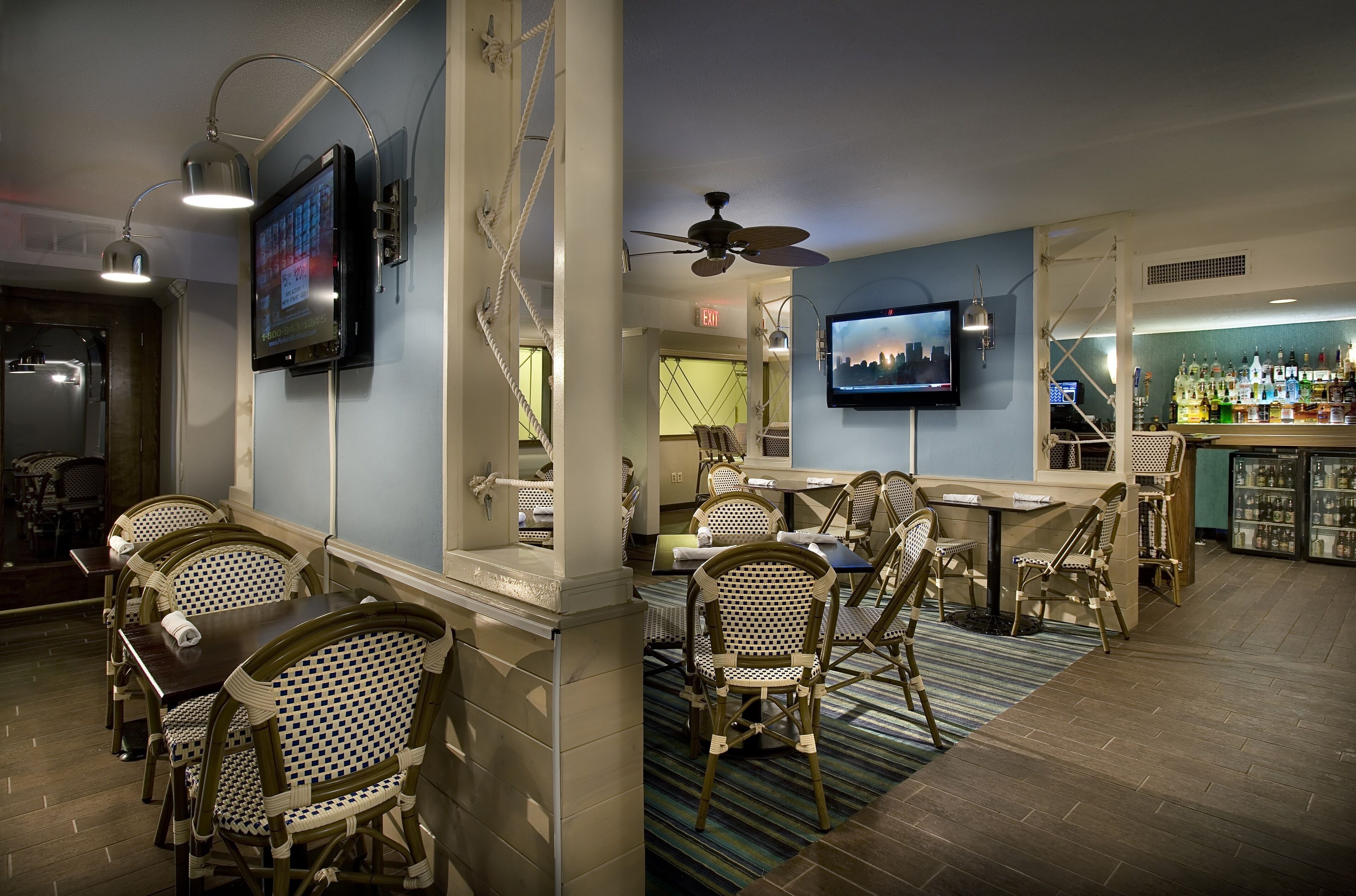 A bar area with wicker chairs and tables, a television mounted on the wall, and a ceiling fan.
