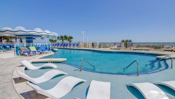 Uma área de piscina com espreguiçadeiras, um espaço de estar coberto e vista desimpedida para a praia.