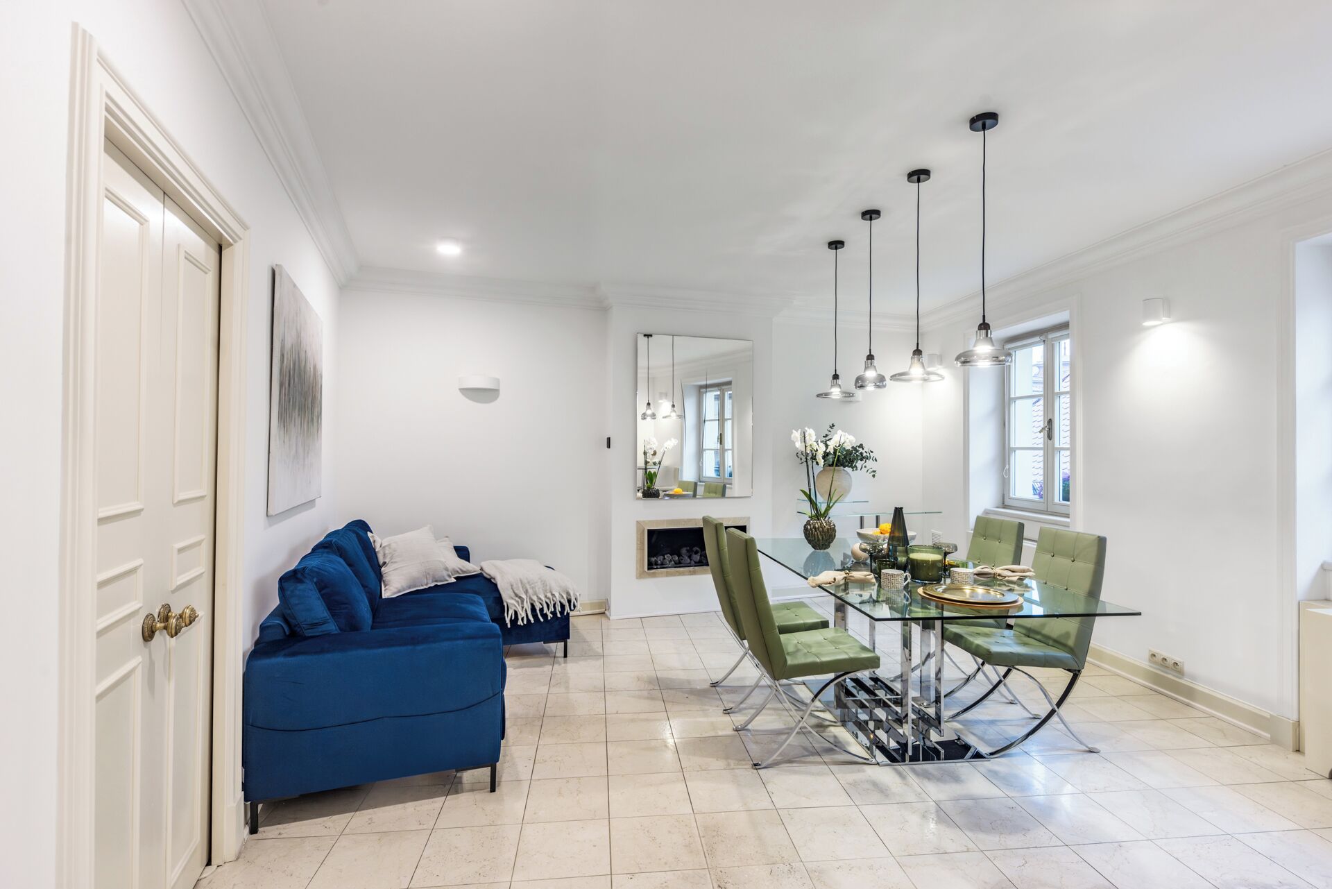 A dining area with a glass table and chairs, a blue sofa, and pendant lighting.