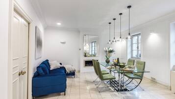 A dining area with a glass table and chairs, a blue sofa, and pendant lighting.