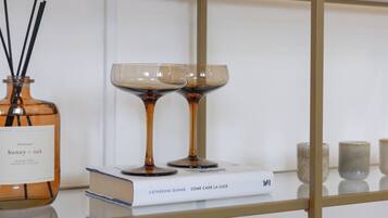 A glass shelf with a bottle of honey + oak, two wine glasses, and a book titled 'Come Cade La Luce' by Catherine Dunne.