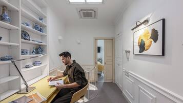 A man sitting at a desk in a room with white walls, a skylight, and shelves with blue and white pottery.