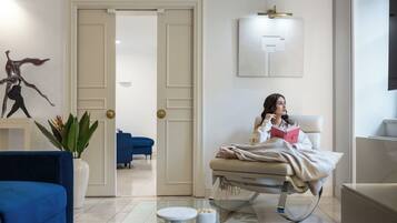 A modern room with a bed, a blue armchair, a white bedside table, and a plant.