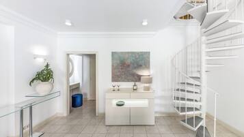 A modern interior with a glass console table, a potted plant, a white console cabinet, a spiral staircase, and a large abstract painting.