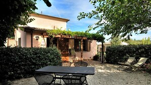 A patio with a table and chairs, a pergola with climbing plants, and a building with a tiled roof. - Apartment GRAPE (Agriturismo Il Corniolo) (CORCIANO)