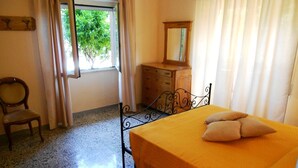 Un dormitorio con cama, cómoda de madera, silla y ventana con cortinas.