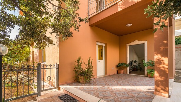 Un patio con piso de baldosas, una reja metálica y plantas en macetas.