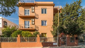 Un edificio de varios pisos con balcones, unidades de aire acondicionado y una entrada protegida por reja.