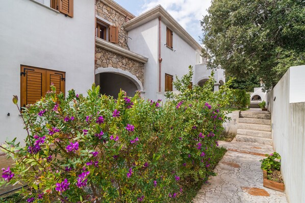 A white building with stone accents, wooden shutters, and a stone staircase leading to a door.
