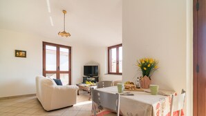 Una sala de estar con un sofá blanco, una mesa de comedor con mantel floreado y un televisor sobre un mueble.