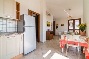Eine Küche mit einem weißen Kühlschrank, Holzschränken und einer gefliesten Spritzschutzwand. Es gibt eine Essecke mit einem Tisch, der mit einer rot-weißen Tischdecke bedeckt ist.