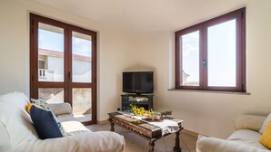Una sala de estar con dos sofás, una mesa de centro, un televisor y ventanas grandes.