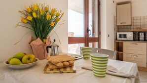 Una cocina con una mesa dispuesta para el desayuno, que incluye pastelería, una cafetera y un bol de fruta.