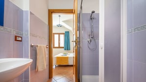 A bathroom with a sink, a shower, and a door leading to a bedroom.