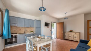 A compact kitchen with blue cabinets, a dining table with chairs, a sofa, and a TV mounted on the wall.