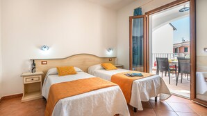A hotel room with two beds, a small table, and a balcony with outdoor furniture.